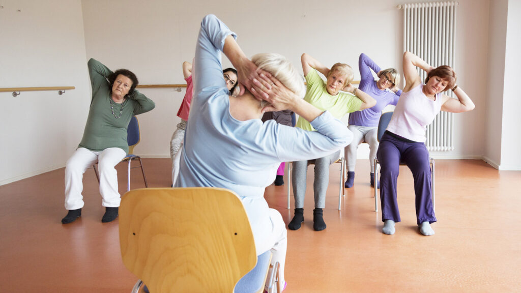 teacher and active senior women yoga class on chairs